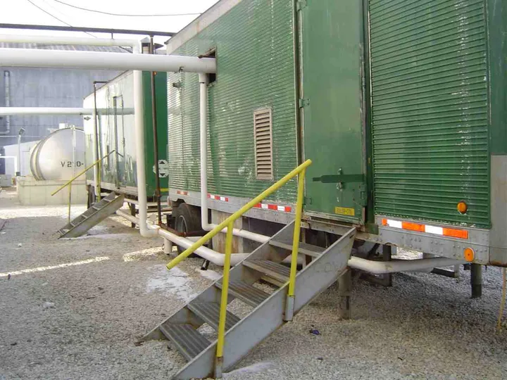 Two green mobile boiler-room trailers with access stairs tied into plant steam piping